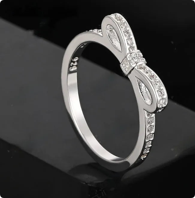 Silver bow-shaped crystal ring with zircon rhinestones on a finger.