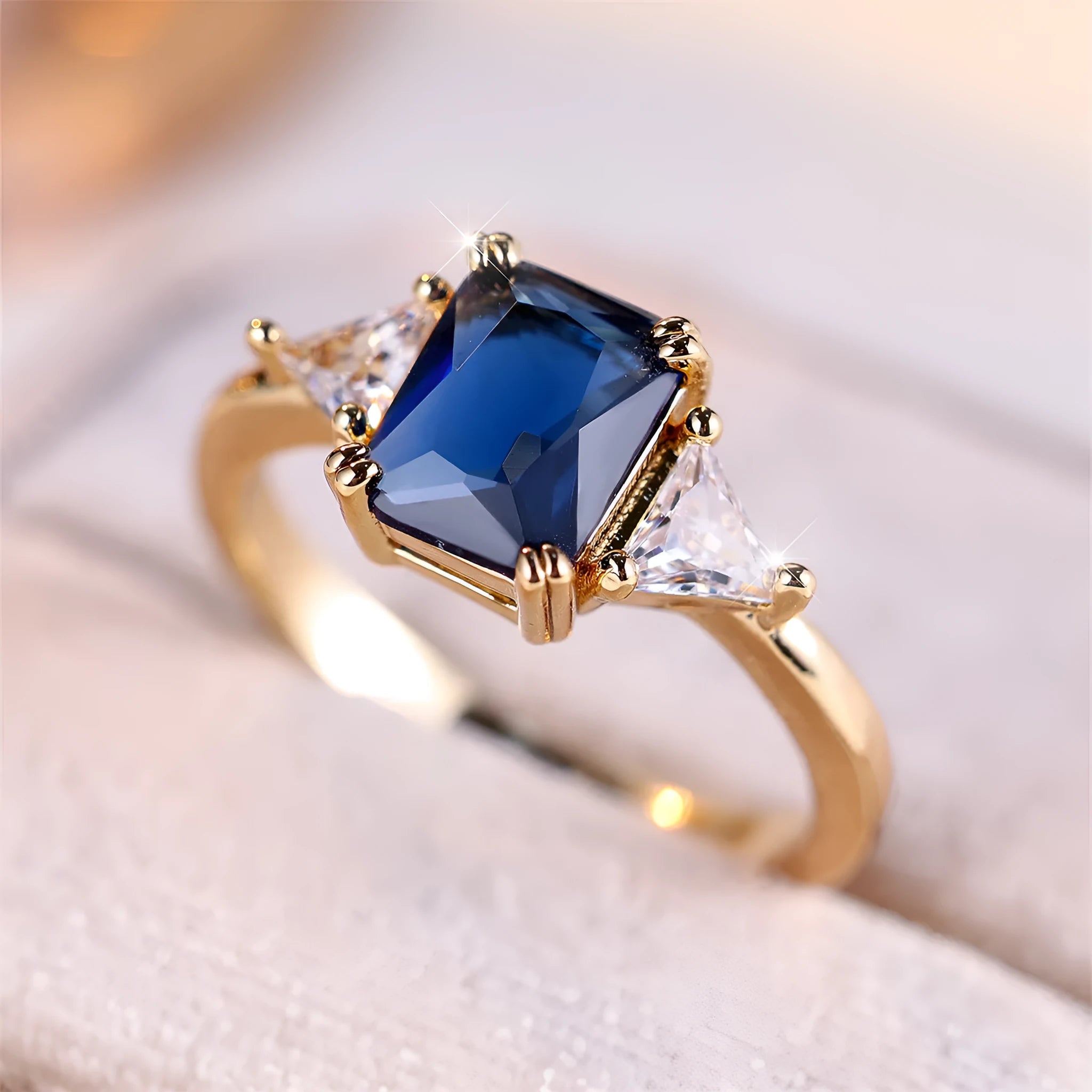 Gold sapphire blue rectangular copper ring for women on plain background