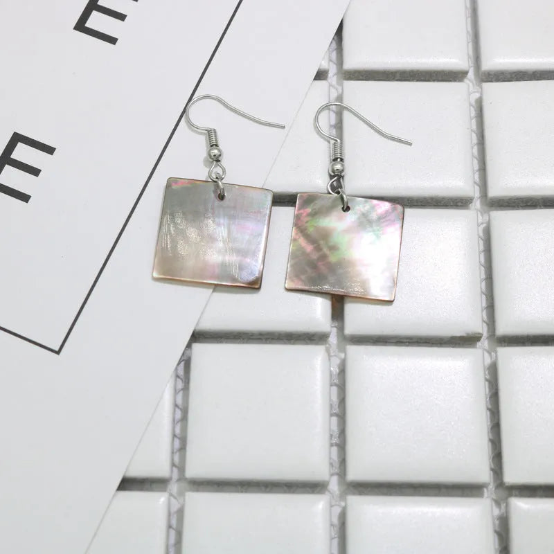 A pair of geometric-shaped shell stud earrings on a plain background, showing the natural texture.