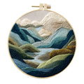 Embroidery DIY kit with cotton landscape fabric, bamboo frame, threads, and tools on wooden surface