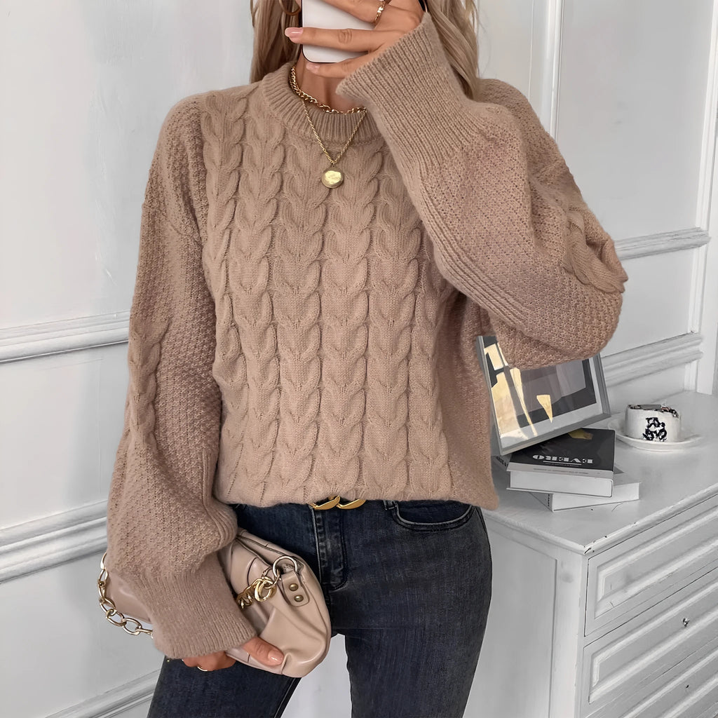 Woman wearing a loose beige round neck sweater with a twisted knit texture detail on the front.