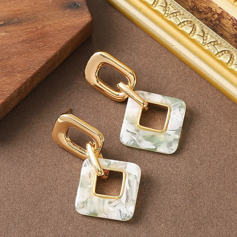 Dignified hollow geometric square copper earrings with electroplated finish on white background