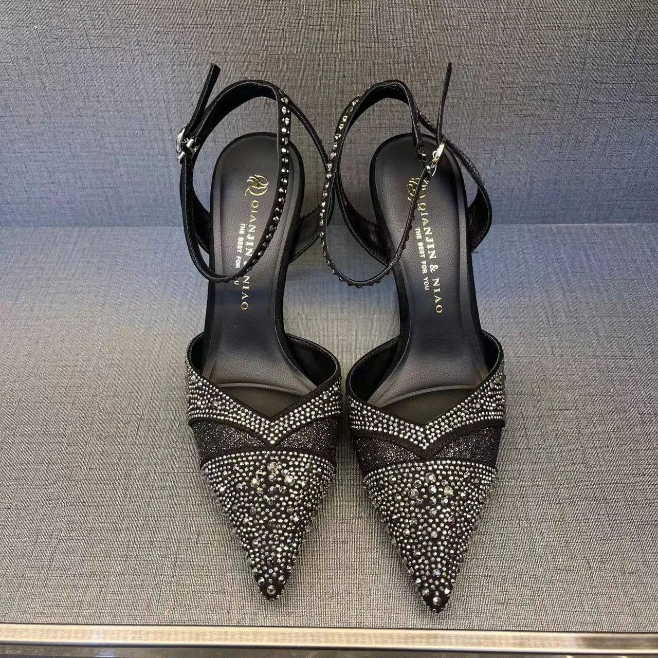 Women's black high heel shoe with pointed toe, stiletto heel, red sole, and hollow design detail.