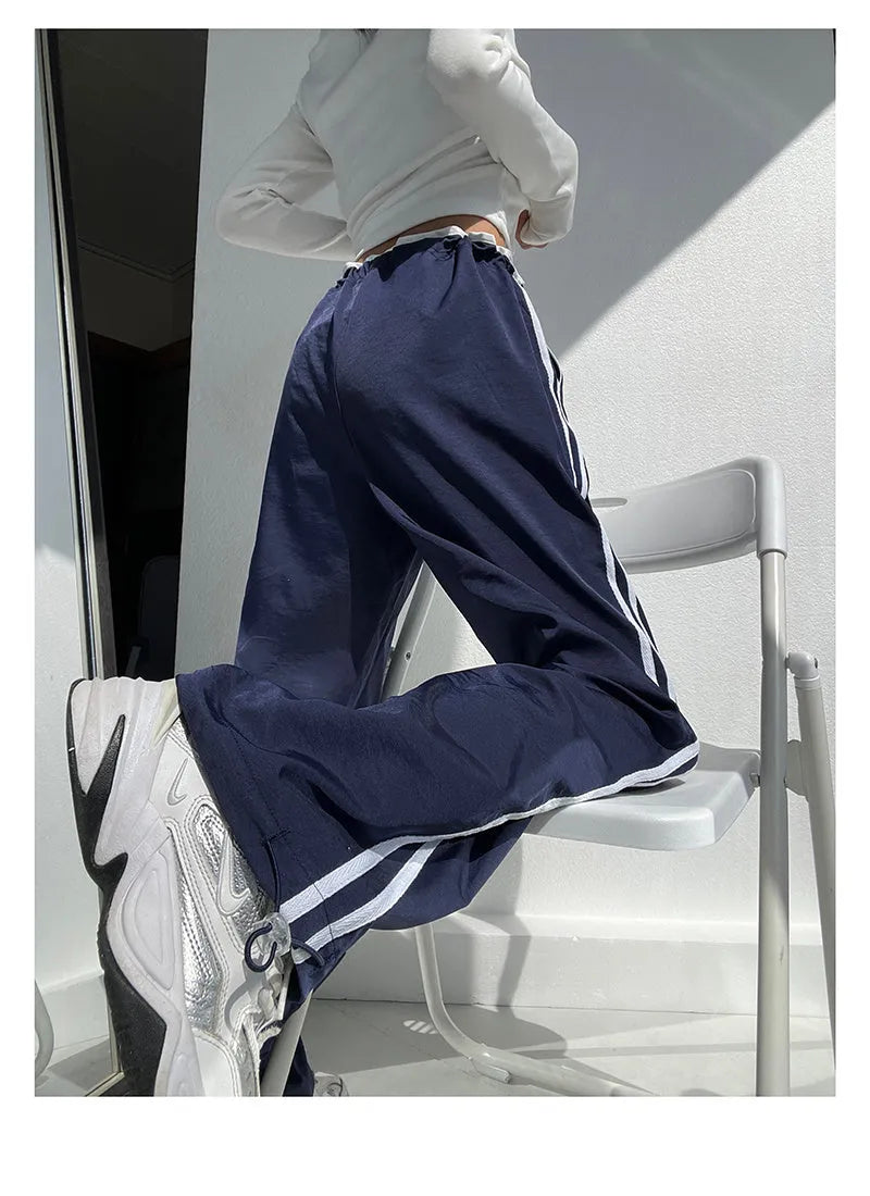 Navy blue loose straight-leg trousers with ribbon parallel bars contrast detail on a hanger.