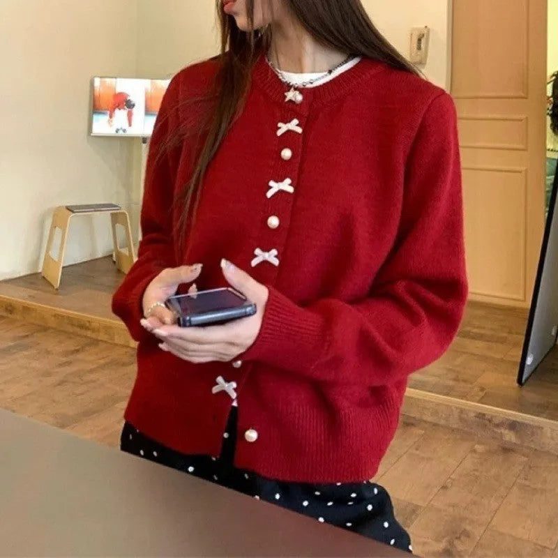 Women's light blue cardigan sweater with a black bow and pearl buttons, open over a white top.