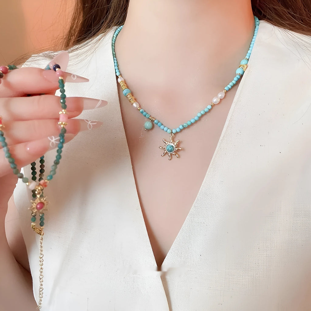 French royal style sun necklace with stone pendant, electroplated finish, and stringed freshwater pearls on a clavicle chain.