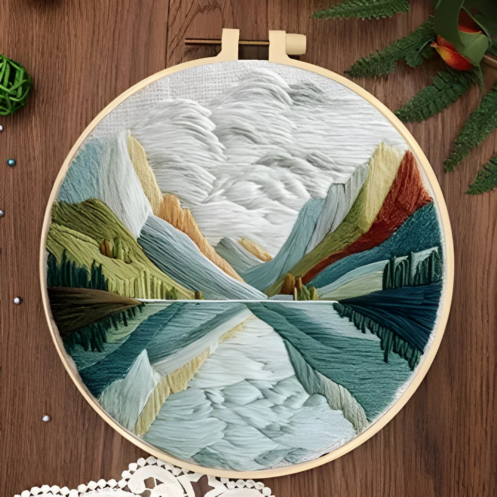 Embroidery DIY kit with cotton landscape fabric, bamboo frame, threads, and tools on wooden surface