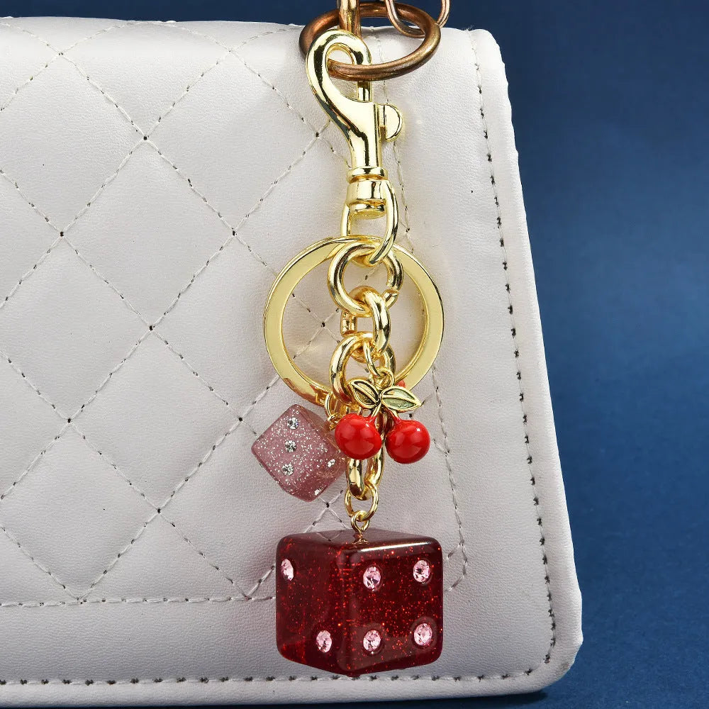 Close-up of a square metal keychain pendant with a vintage cherry two-tone dice pattern.