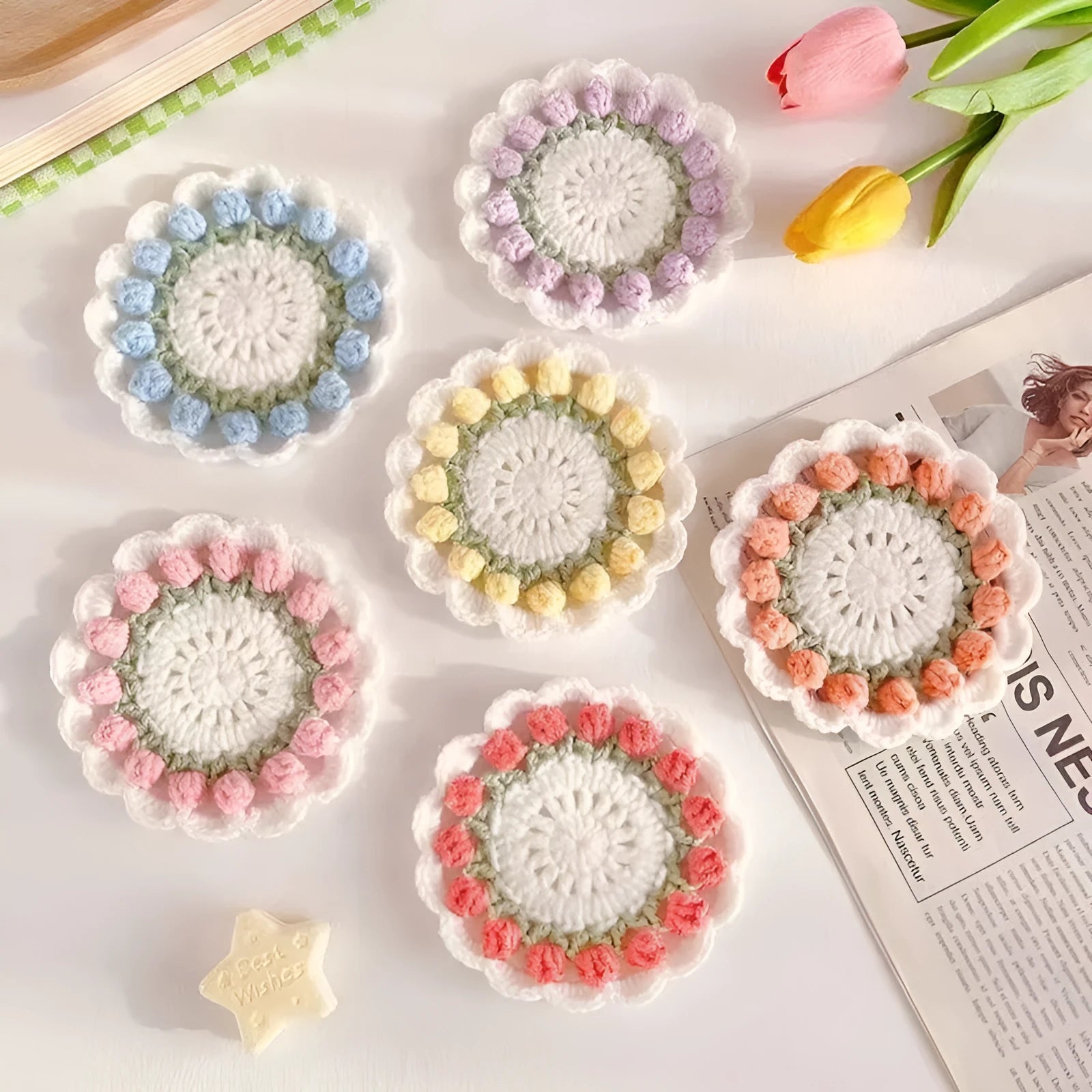 Handmade yarn hook woven flower coaster in pink on a wooden table next to a glass of water