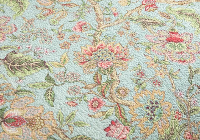 Blue cotton bedspread set with American floral and bird pattern laid on a bed.