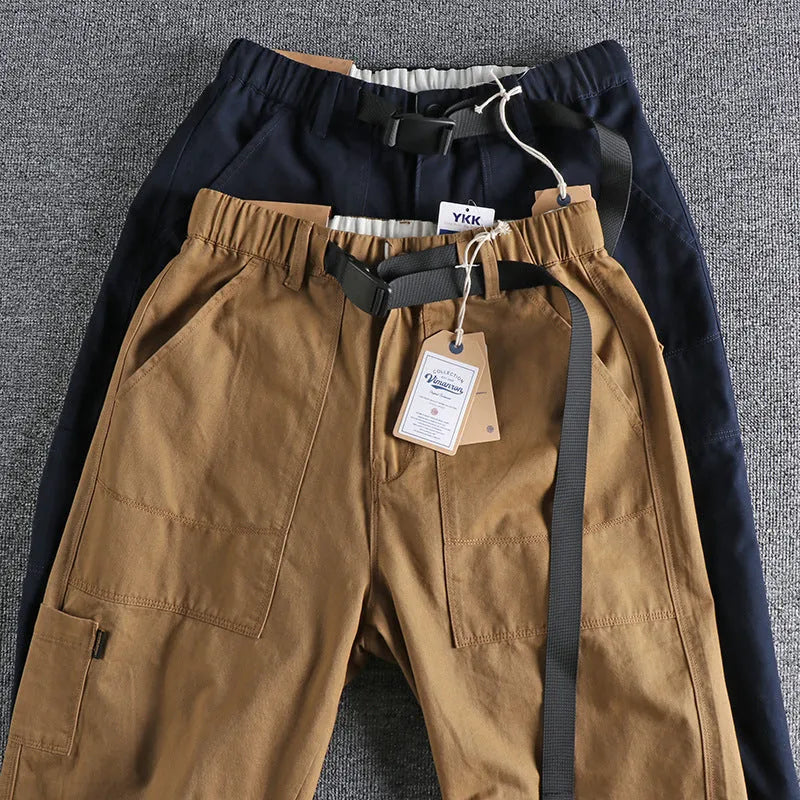 Men's khaki trousers with N buckle belt closure and zipper fly on a mid-waist fit.