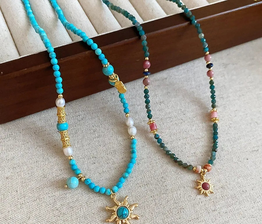 French royal style sun necklace with stone pendant, electroplated finish, and stringed freshwater pearls on a clavicle chain.