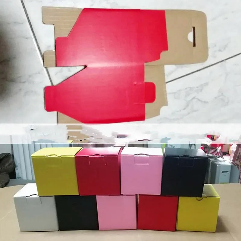 Square corrugated cardboard packaging box in black, shown alongside smaller white and grey boxes.