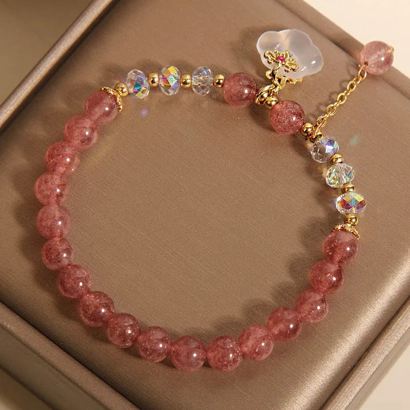 Women's natural strawberry quartz and white agate crystal bracelet with auspicious cloud pattern on a flat surface