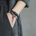 Black hair crystal bracelet with white crystal tassel and bending and lacing design on neutral background