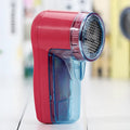 Handheld portable electric lint and pill remover for sweaters on a blue background.