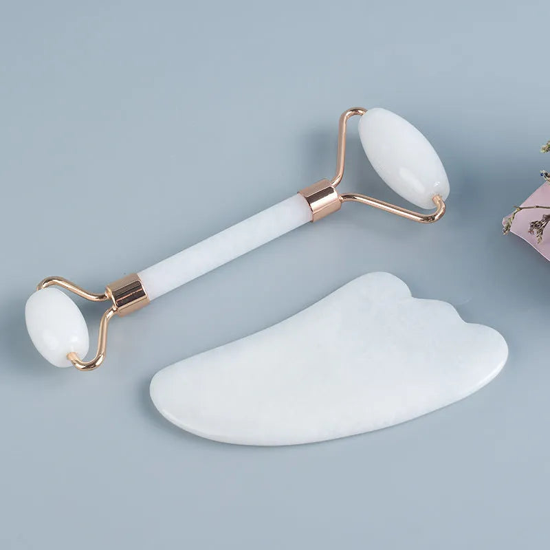 White jade facial roller and gua sha board set on a neutral background.