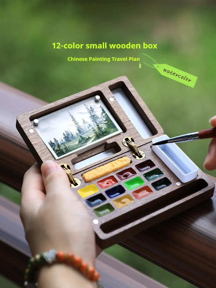 Mini wooden watercolour paint box open to show compartments filled with professional artist pigments.