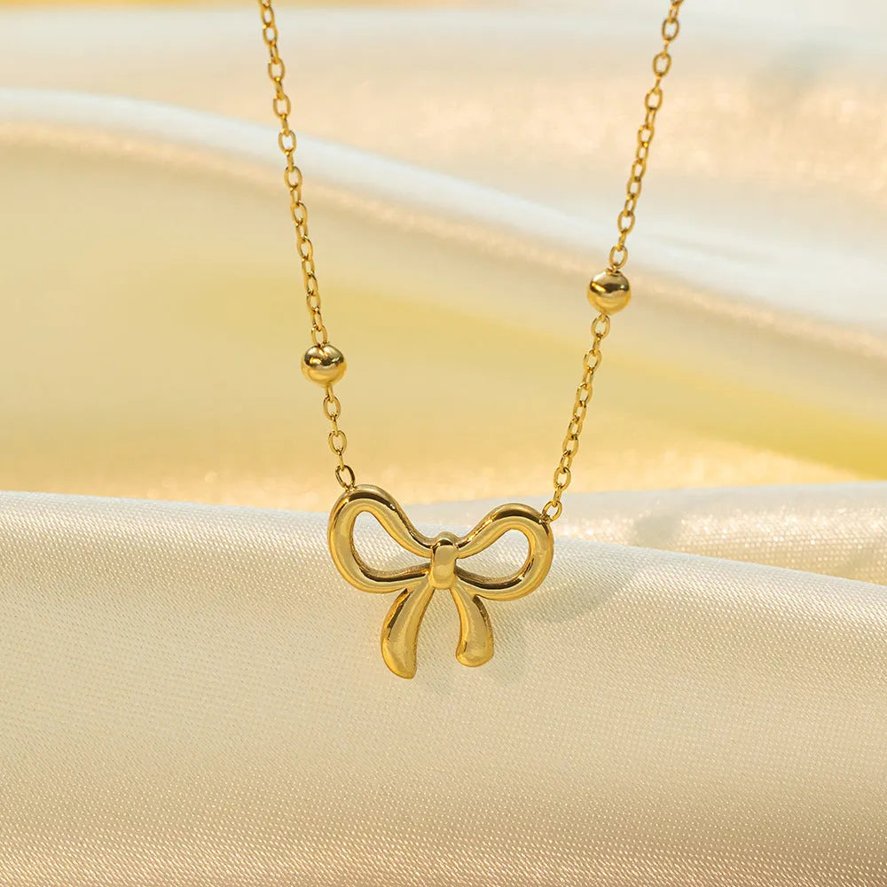 Gold titanium steel bow necklace with cross chain design on display