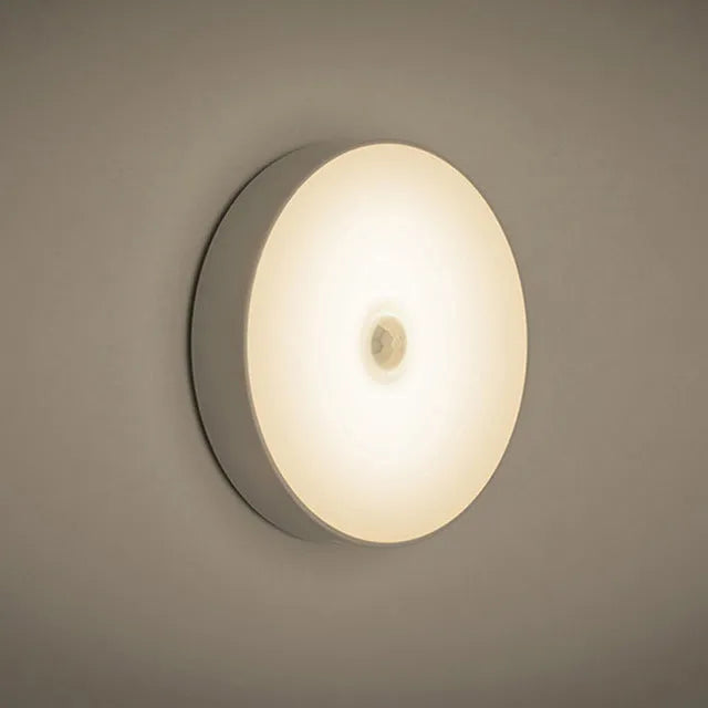 Small round white LED night light with motion sensor, shown with USB charging cable and adhesive tape.