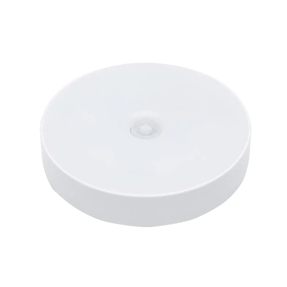 Small round white LED night light with motion sensor, shown with USB charging cable and adhesive tape.