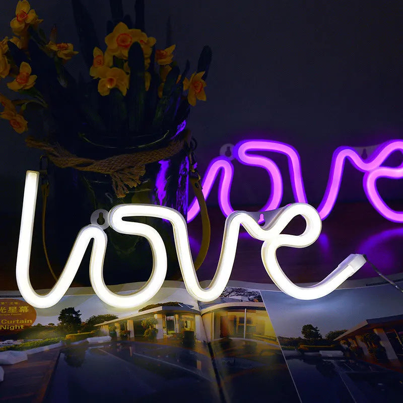 Pink love-shaped LED neon sign light on a table with USB cable and batteries.