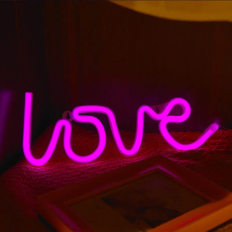 Pink love-shaped LED neon sign light on a table with USB cable and batteries.