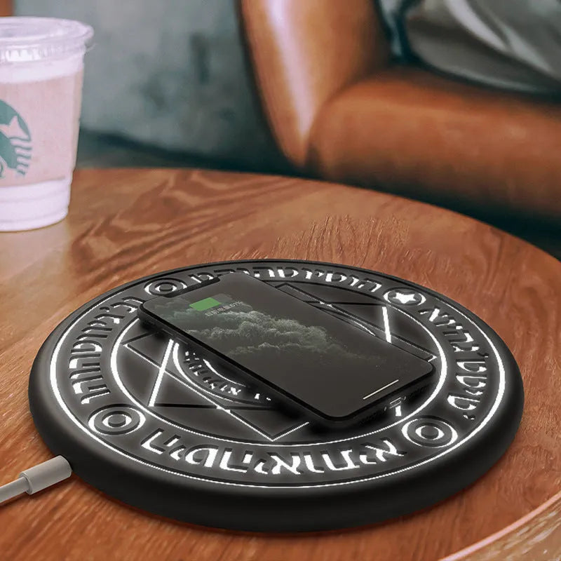 Square black wireless charging pad with illuminated magic array pattern, shown with a smartphone on top.