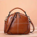 Round leather handbag with zipper opening and soft double handles in wine red colour.