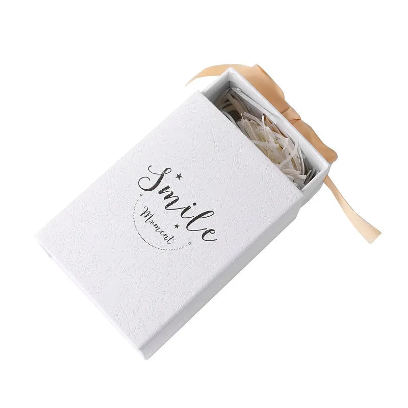 Small cardboard gift box with bronzing detail, handbag, and raffia on a white background