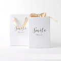 Small cardboard gift box with bronzing detail, handbag, and raffia on a white background