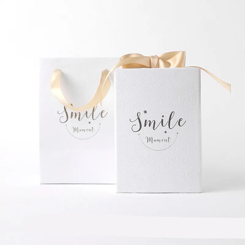 Small cardboard gift box with bronzing detail, handbag, and raffia on a white background