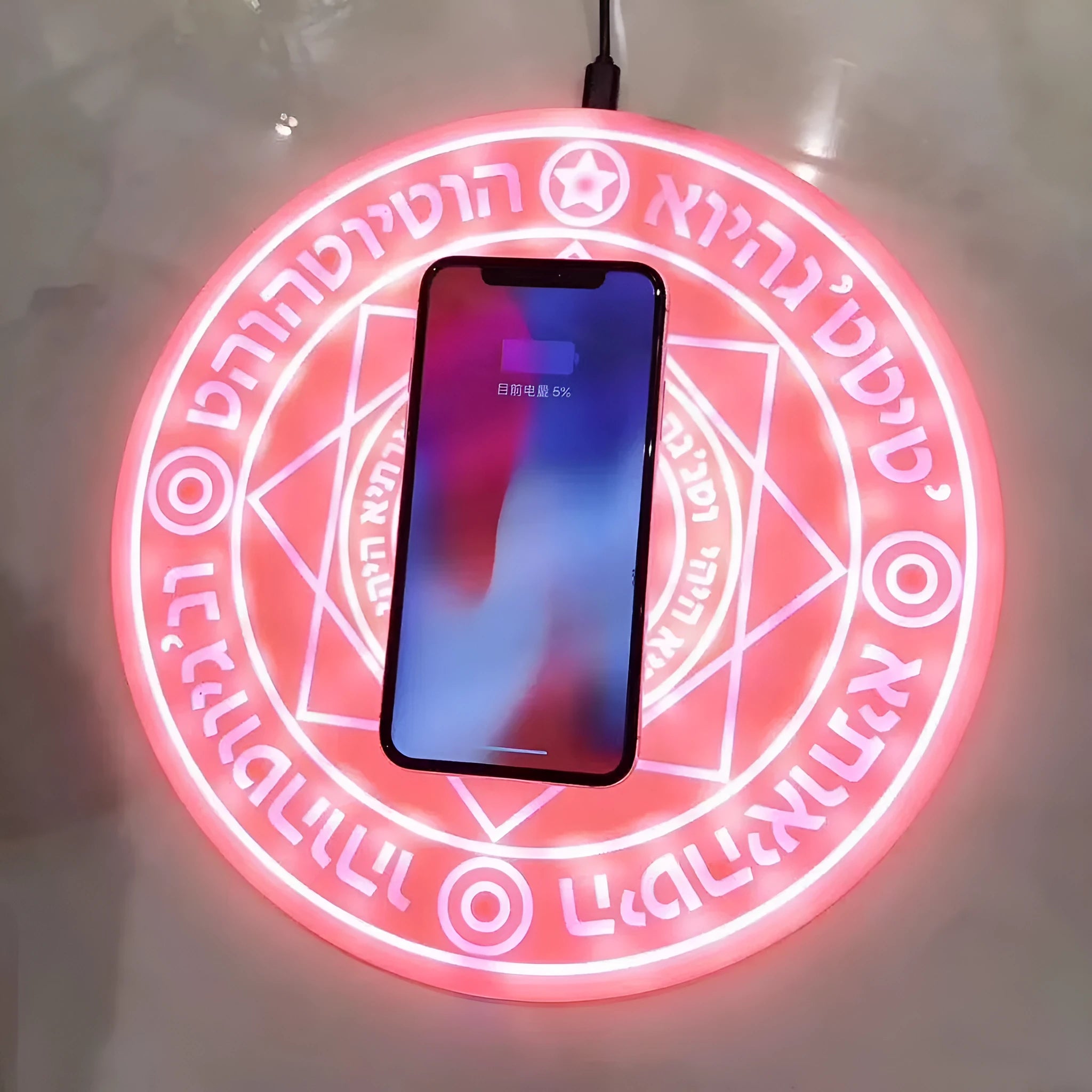 Square black wireless charging pad with illuminated magic array pattern, shown with a smartphone on top.