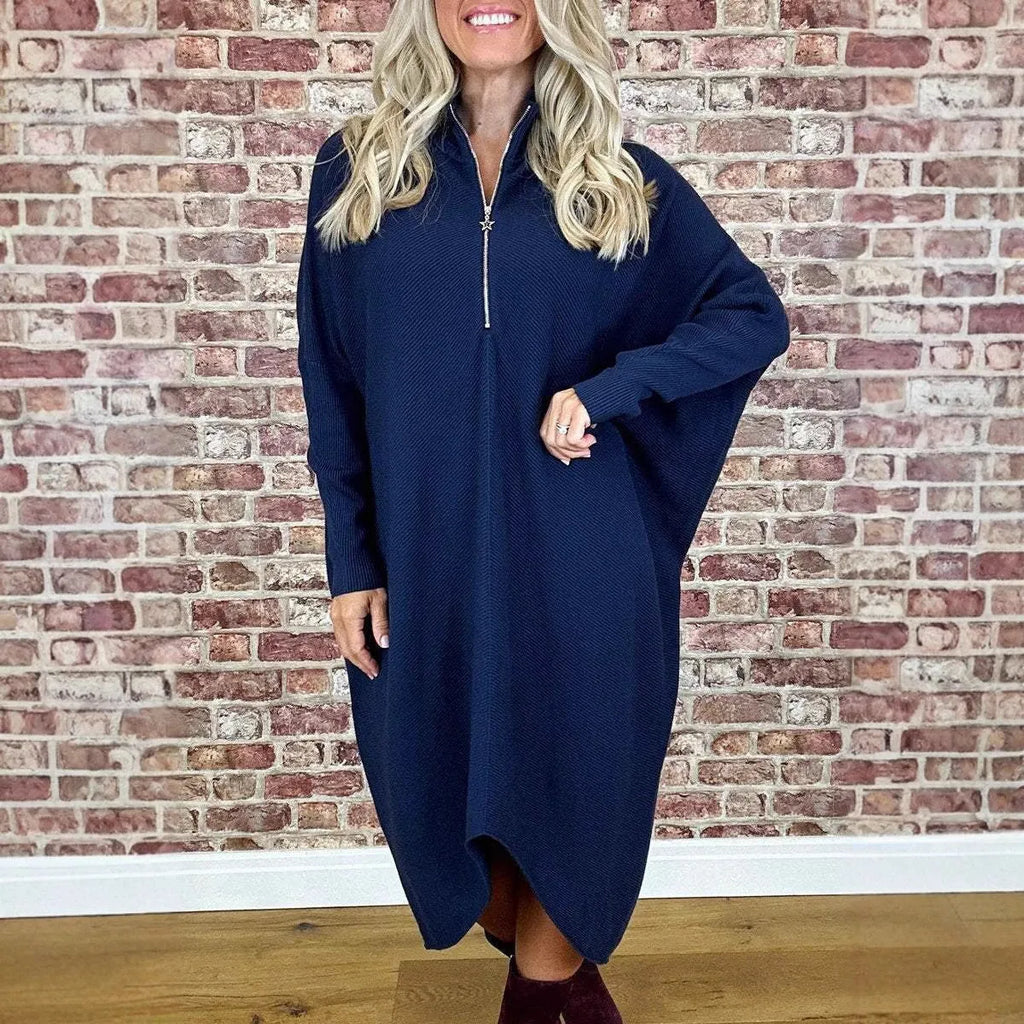 A woman modelling a loose-fitting dark green knitted dress with a front zipper detail and raglan sleeves.