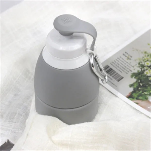 Silicone folding water bottle 580ml in blue, collapsed and full size, with cap, on outdoor background
