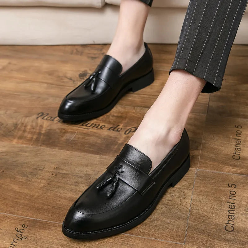 Men's black slip-on business casual shoes with a tassel detail and pointed toe on a rubber sole.