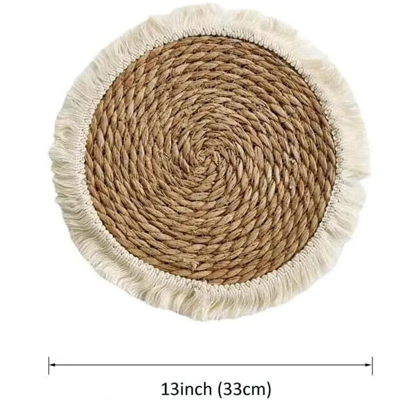 A round natural papyrus placemat with decorative tassels, shown on a wooden table.