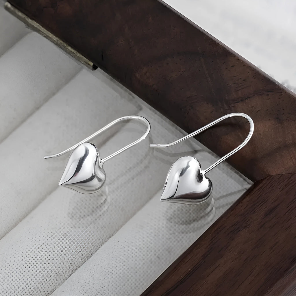 Close-up of glossy silver three-dimensional heart-shaped earrings on a white background.