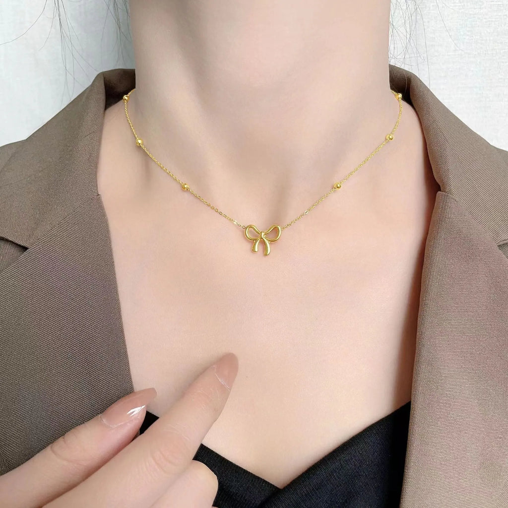 Gold titanium steel bow necklace with cross chain design on display