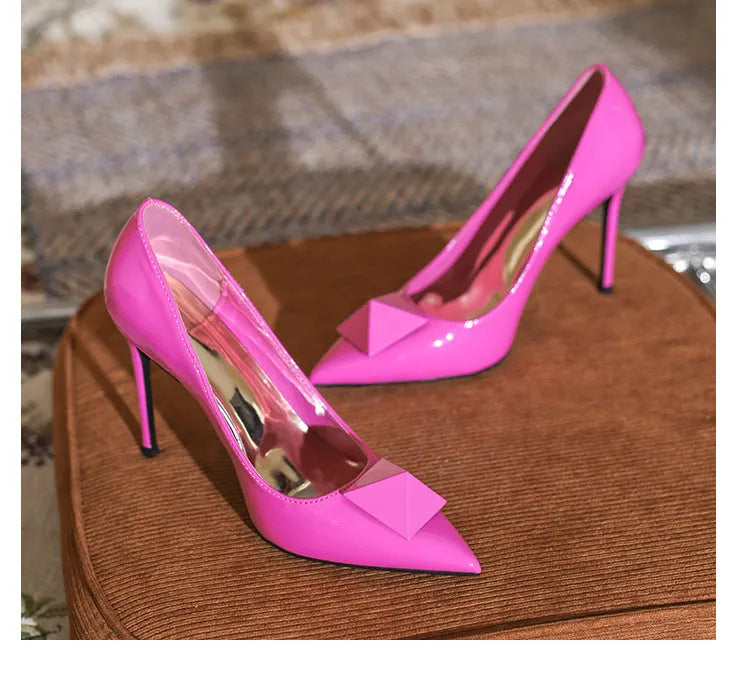Pink women's patent leather pointed toe stiletto heels with a buckle, shown on a white background.