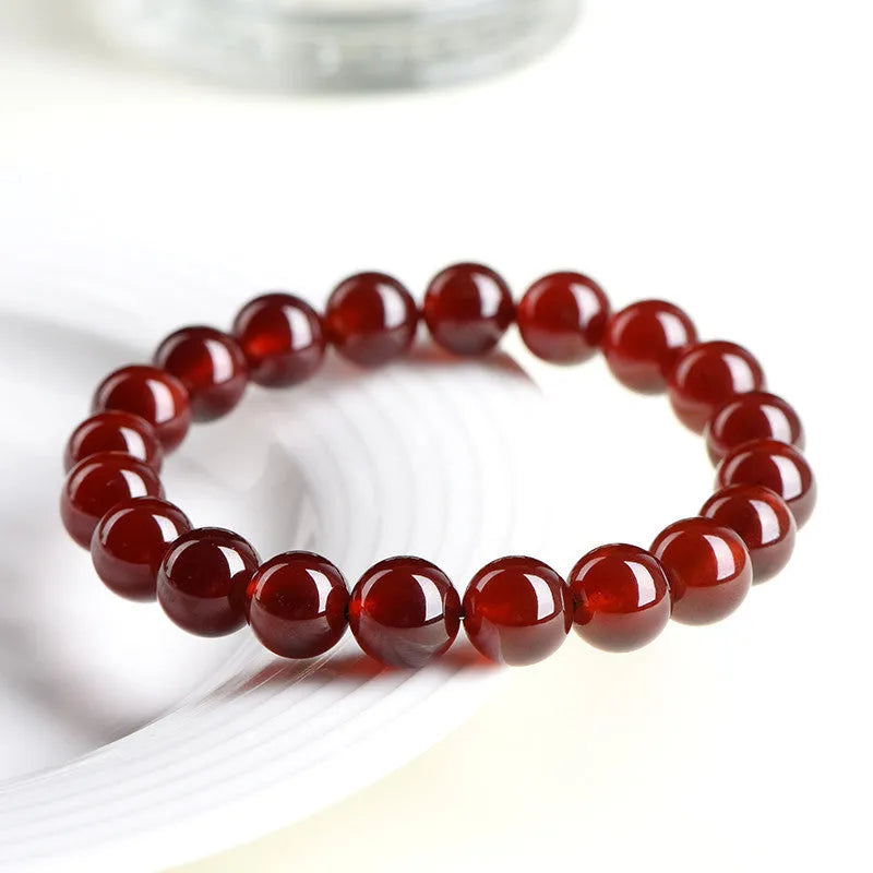 Natural orange red garnet ball bracelet with a silver ruyi charm on a white background.