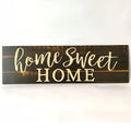 Home Sweet Home wooden carved pendant in black, 40cm x 12cm, hanging on a light wall