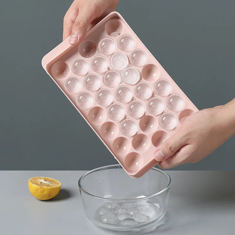 Round ball ice cube tray in sky blue with 33 grids, empty and filled with water, on a kitchen countertop