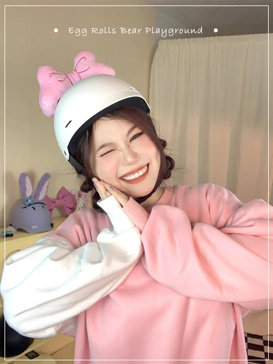 Plush bow tie helmet decoration in red, peach pink, and rose pink colours shown on a motorcycle helmet.