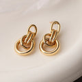 A pair of gold-coloured geometric copper earrings with irregular shapes on a white background.
