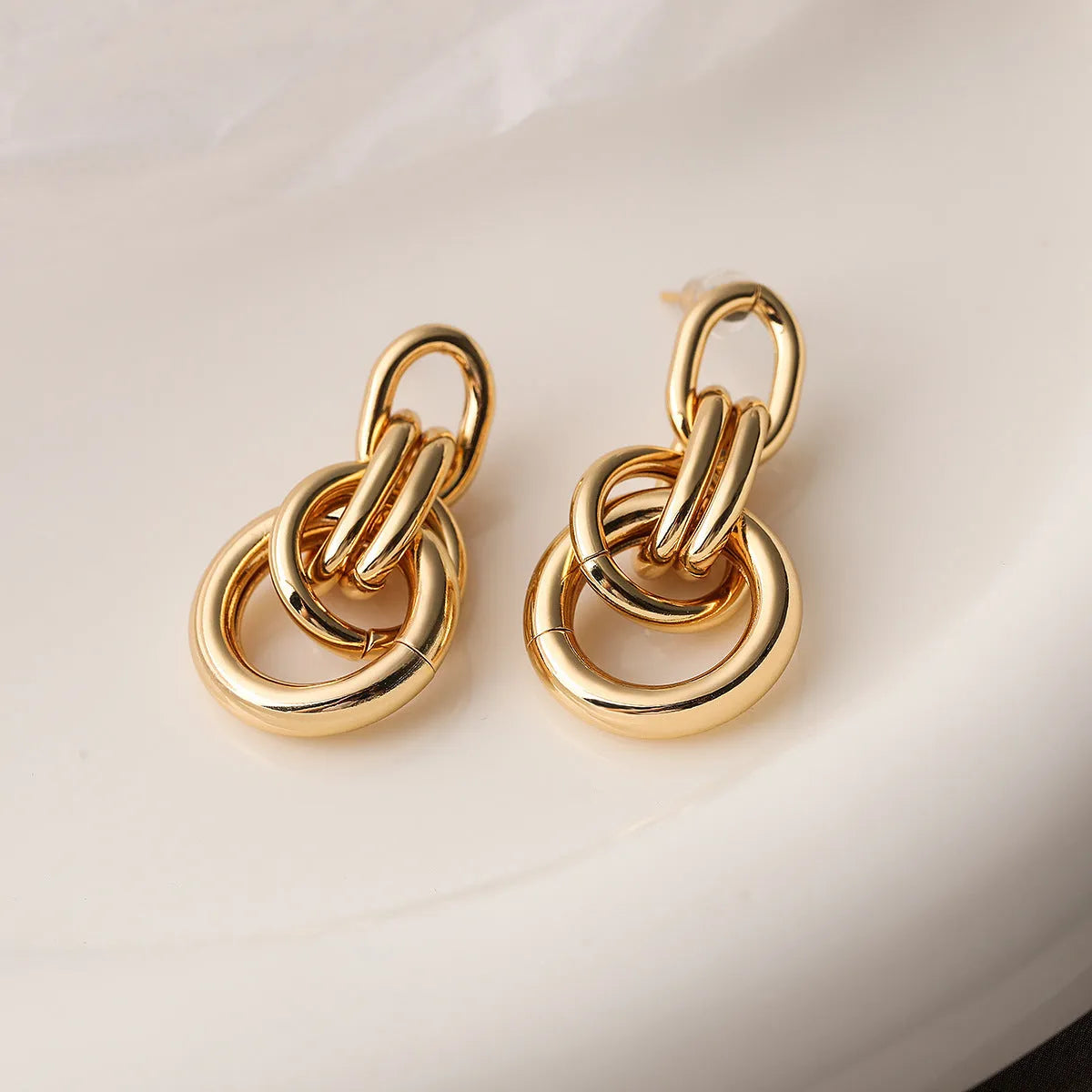 A pair of gold-coloured geometric copper earrings with irregular shapes on a white background.