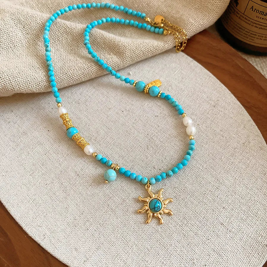 French royal style sun necklace with stone pendant, electroplated finish, and stringed freshwater pearls on a clavicle chain.