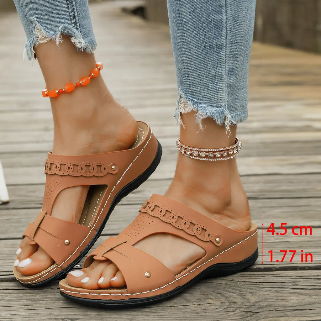 Pair of beige Roman style slippers with a fish mouth toe and slope heel on a rubber sole.