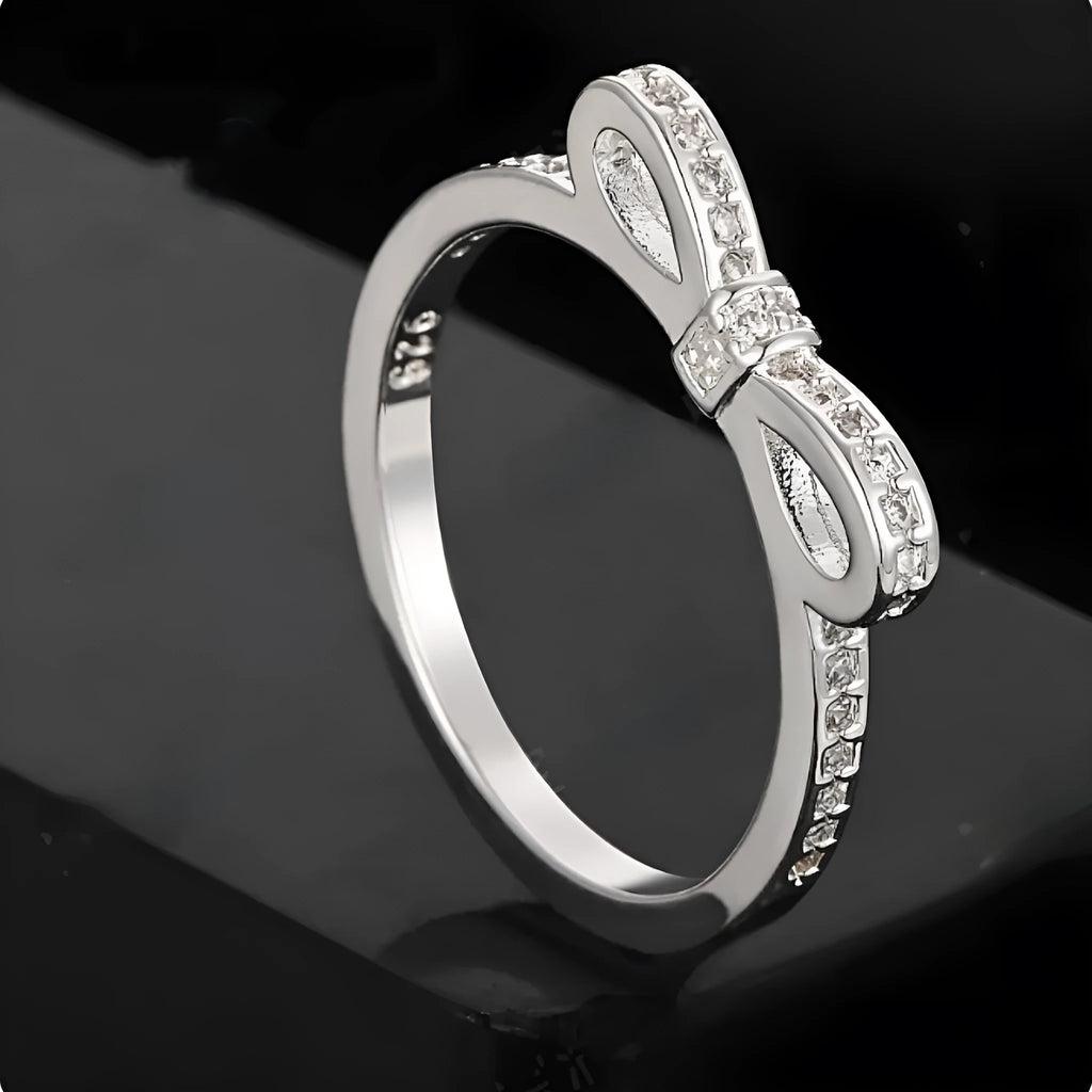 Silver bow-shaped crystal ring with zircon rhinestones on a finger.