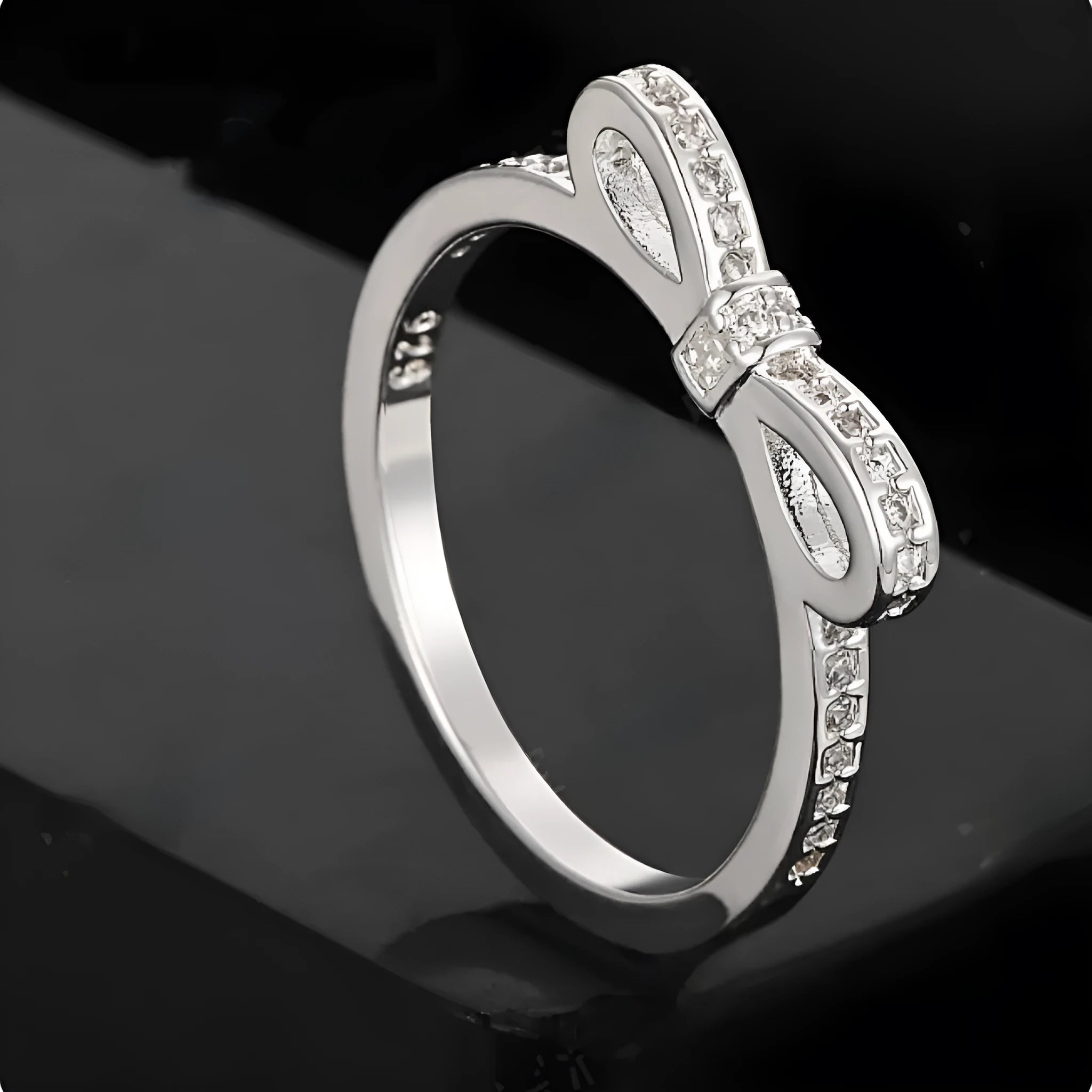 Silver bow-shaped crystal ring with zircon rhinestones on a finger.